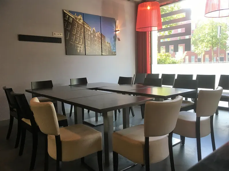 Tafelopstelling met tafels aan elkaar en stoelen eromheen, bij het grote raam